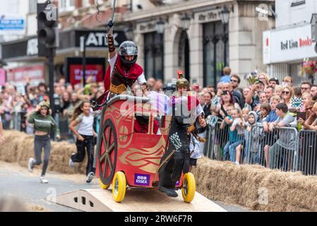 High Street, Colchester, Essex, Großbritannien. September 2023. In der historischen Stadt Colchester findet die erste Seifenkasten-Rallye statt, an der rund 50 Teilnehmer teilnehmen. Die Karts werden über eine Rampe gestartet, um ihnen die Geschwindigkeit zu geben, den Kurs entlang der High Street zu bewältigen, die verschiedene Hindernisse enthält, bevor die Fahrer die Ziellinie erreichen. Römisches Wagenteam in Bezug auf Colchesters römische Geschichte Stockfoto