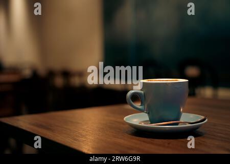Kaffee in blauer Tasse auf einem Holztisch im Café mit beleuchtetem Hintergrund Stockfoto