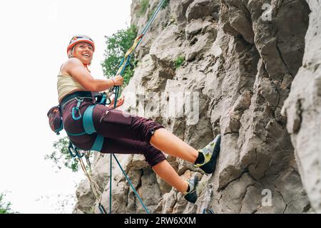 Lächelnde Sportlerin in Schutzhelm und -Schuhen Klettern auf die Felswand mit Seil und Gurtzeug im Paklenica-Nationalpark in Kroatien. Stockfoto