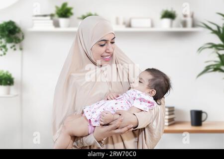 Porträt einer lächelnden jungen muslimischen Mutter, die Hijab trägt und ihr süßes kleines Baby hält. Stockfoto