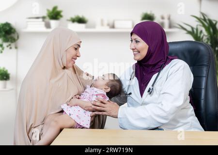 Glückliche junge muslimische Mutter, die mit ihrem süßen kleinen Baby einen allgemeinen Kinderarzt in einer modernen Klinik für Routineuntersuchungen, Gesundheitswesen und Medizin besucht Stockfoto