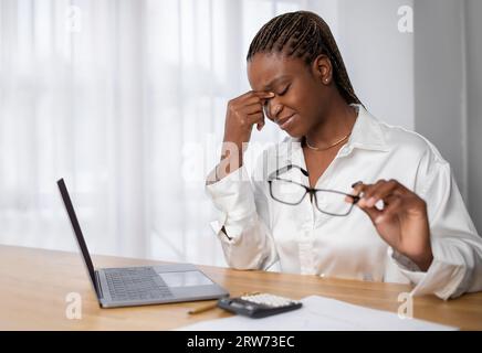 Erschöpfte junge schwarze Frau, die im Büro arbeitet Stockfoto
