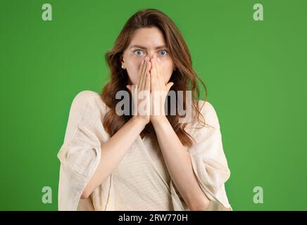 Verängstigte junge europäische Dame in lässigen Hüllen Gesicht mit Händen, isoliert auf grünem Studiohintergrund Stockfoto