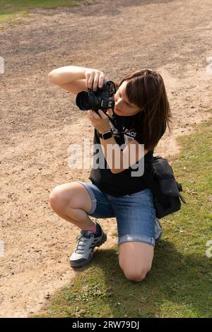 Junge Fotografin kniet beim Fotografieren mit DSLR-Kamera im Freien Stockfoto