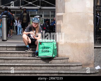 Uber isst Fahrradkurierfahrerin, die etwas Essen isst, während sie in Central London auf Bestellungen wartet Stockfoto