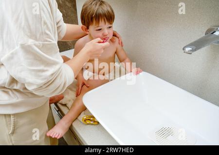 Baby und seine Mutter putzen sich die Zähne im Badezimmer. Kind im Alter von zwei Jahren (zweijähriger Junge) Mutter hilft Kind, ihre Zähne mit einer Zahnbürste zu putzen Stockfoto