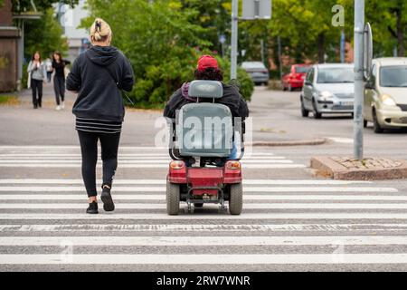Person in einem elektrischen Rollstuhl, die eine Straße überquert Stockfoto