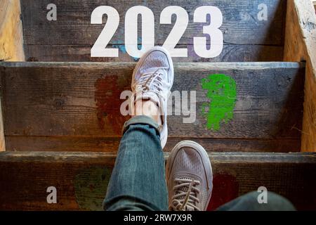 Frauenbeine auf einer Holztreppe und der Text 2023 auf den Stufen, gehen die Treppe hinunter, frohes neues Jahr 2023, gehen Sie in das neue Jahr Stockfoto