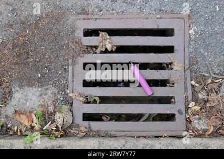 Ein lila E-Zigarettenvape wurde entsorgt und liegt auf einer Metallabdeckung für den Wasserablauf. Stockfoto