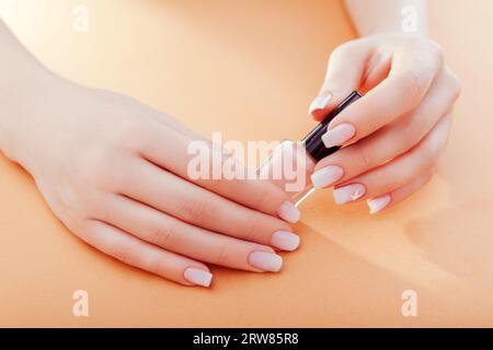 Ombre französische Maniküre auf orangefarbenem Hintergrund. Nahaufnahme der Nagelkunst auf Fingernägeln. Frau hält nagellack. Ich kümmere mich um die Hände Stockfoto