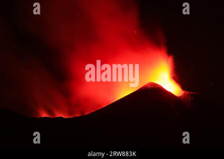 L'Etna in un'eruzione lavica notturna con cratere sagomato in controluce e grandi emissioni di fumo in una vista panoramica del vulcano siciliano Stockfoto