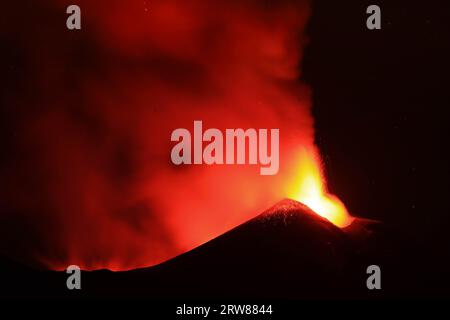 L'Etna in un'eruzione lavica notturna con cratere sagomato in controluce e grandi emissioni di fumo in una vista panoramica del vulcano siciliano Stockfoto