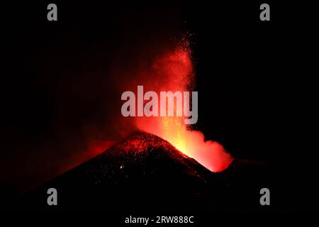 L'Etna in un'eruzione lavica notturna con cratere sagomato in controluce e grandi emissioni di fumo in una vista panoramica del vulcano siciliano Stockfoto