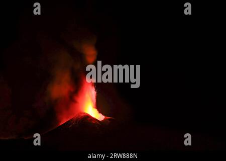 L'Etna in un'eruzione lavica notturna con cratere sagomato in controluce e grandi emissioni di fumo in una vista panoramica del vulcano siciliano Stockfoto