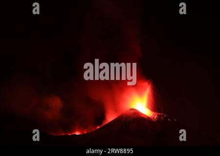 L'Etna in un'eruzione lavica notturna con cratere sagomato in controluce e grandi emissioni di fumo in una vista panoramica del vulcano siciliano Stockfoto