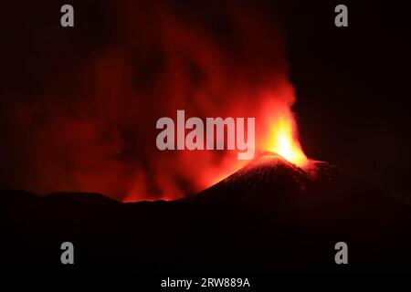 L'Etna in un'eruzione lavica notturna con cratere sagomato in controluce e grandi emissioni di fumo in una vista panoramica del vulcano siciliano Stockfoto