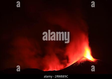 L'Etna in un'eruzione lavica notturna con cratere sagomato in controluce e grandi emissioni di fumo in una vista panoramica del vulcano siciliano Stockfoto