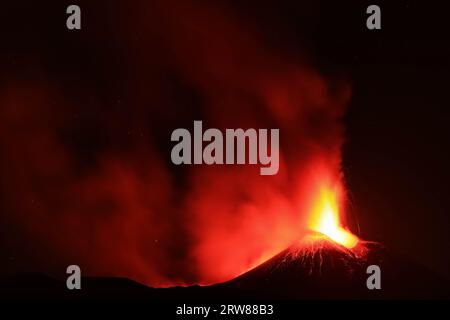 L'Etna in un'eruzione lavica notturna con cratere sagomato in controluce e grandi emissioni di fumo in una vista panoramica del vulcano siciliano Stockfoto