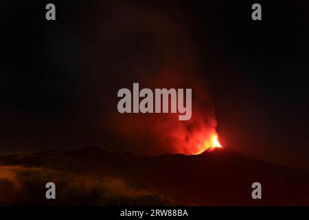 L'Etna in un'eruzione lavica notturna con cratere sagomato in controluce e grandi emissioni di fumo in una vista panoramica del vulcano siciliano Stockfoto