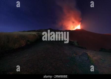 Ätna - suggestive Eruption mit sanften Lichtern während einer Lavaexplosion im Krater mit Emission von Asche und mit dem Sternenhimmel im Hintergrund Stockfoto