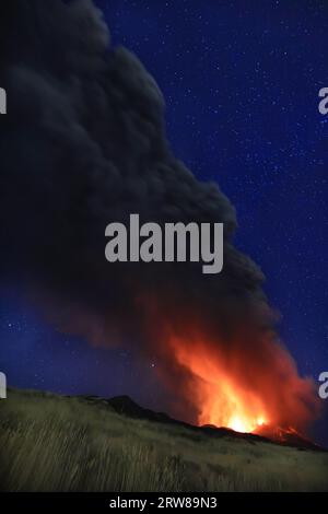 Ätna eruzione in Sicilia con vista panoramica della grande colonna di fumo e cenere dal cratere vulcano nel ciel notturno stellato del Agosto 2023 Stockfoto