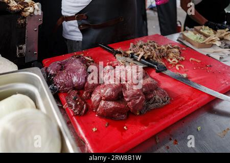 Selektiver Fokus auf den Stapel rohes Rindfleisch in Scheiben auf rotem Schneideblock auf der Theke im Freien am Street Food Beef Steak Stand. Stockfoto