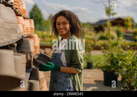 Frau Gärtnerin, die in der Nähe von Regalen voller leerer Blumentöpfe im Gartencenter steht Stockfoto