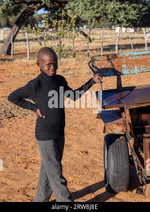 Junger afrikanischer Dorfjunge, der den Griff eines handgefertigten Wagens hält, der von Tieren gezogen wird Stockfoto