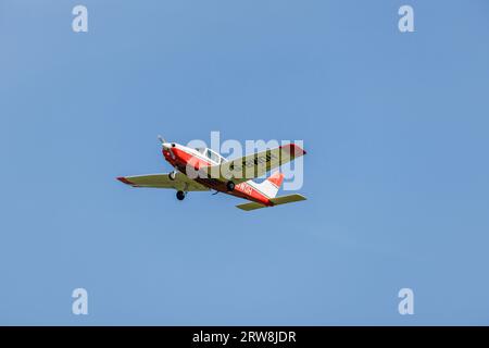 Ein rot-weißes Piper PA-28-161 Cadet-Leichtflugzeug im Flug, das nach dem Start vom Flughafen Fairoaks in Chobham, Surrey, aufsteigt Stockfoto