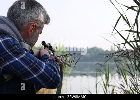 Mann mit Jagdgewehr in der Nähe des Sees im Freien. Leerzeichen für Text Stockfoto