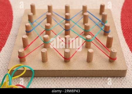 Geobord aus Holz mit Gummibändern auf Teppich, Nahaufnahme. Lernspielzeug für die Entwicklung motorischer Fähigkeiten Stockfoto