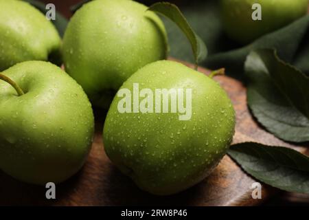 Reife grüne Äpfel mit Blättern und Wassertropfen auf Holzbrett, Nahaufnahme Stockfoto