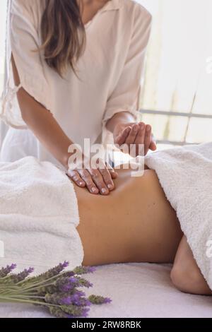 Masseurin mit Patientin auf Massagetisch, die Öl auf ihren Bauch legt, Nahaufnahme unbekannter Menschen. Stockfoto