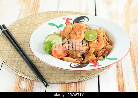 Meeresfrüchte Kwetiau Goreng mit Ei, Garnelen, Fischfleischbällchen und Limette. Gebratenes Char Kway Teow mit Garnele auf weißem Tisch Stockfoto