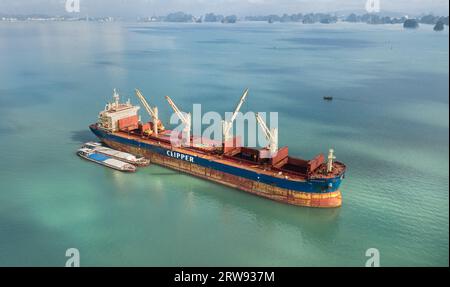 Das Massengutschiff Clipper Kythira ankerte in der Halong-Bucht (Hạ Long), Vietnam, und entlädt Fracht in lokale Frachtschiffe zwischen touristischen Kalksteinklippen Stockfoto