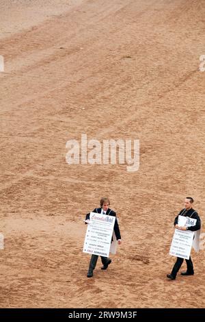 Mark Jenkins und General Manager des Cavendish Hotels James Ryder tragen Sandwichbretter am Torre Abbey Beach und filmen die Serie 4 des Hotels Stockfoto