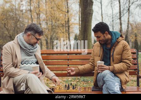 Multiethnische Männer spielen Schach im Herbstpark auf einer Bank. Stockfoto