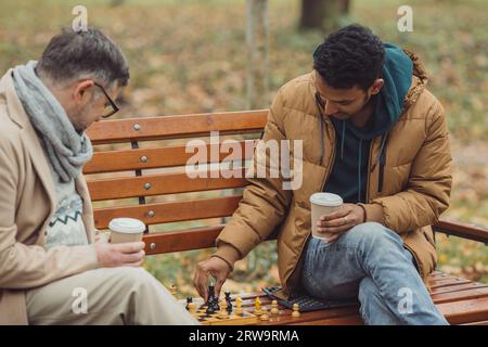 Multiethnische Männer spielen Schach im Herbstpark auf einer Bank. Stockfoto