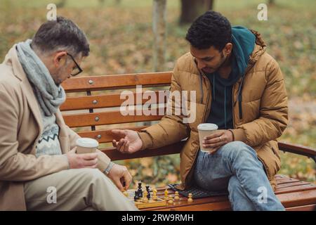 Multiethnische Männer spielen Schach im Herbstpark auf einer Bank. Stockfoto