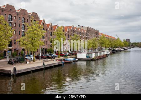 Gebäude am Kanal und am Kai sowie von Entrepotdok in Amsterdam, die von alten Lagerhäusern in Wohnungen, Büros und Cafés in Holland, Niederlande, umgewandelt wurden Stockfoto