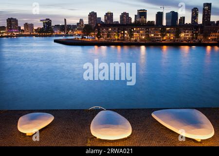 Skyline der Stadt Rotterdam in der Abenddämmerung und Promenade entlang des Flusses mit beleuchteten Bänken, Südholland, Niederlande Stockfoto