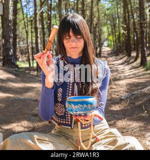Nahaufnahme einer Frau, die eine tibetische Klangschale im Wald spielt Stockfoto
