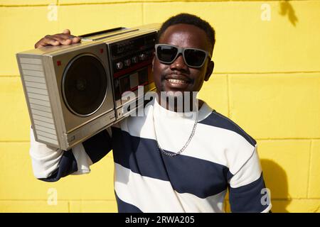 Lebendiges Porträt des funky Black man, der draußen die Box hält und die Kamera anlächelt Stockfoto