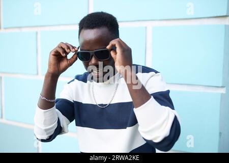 Hüfthohes Porträt des funky schwarzen Mannes, der eine Sonnenbrille in der Stadt auf blauem Kopienraum trägt Stockfoto