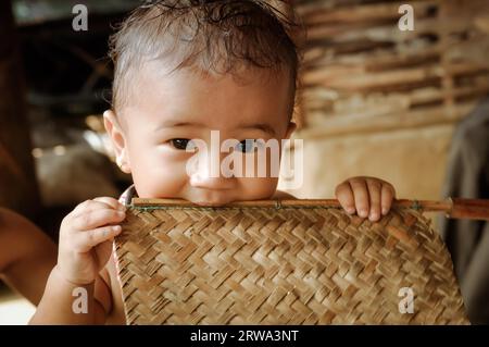 Damak, Nepal, um Mai 2012: Foto eines kleinen süßen Jungen, der auf eine Fotokamera schaut und im nepalesischen Flüchtlingscamp in Damak einen Holzstab in den Mund hält Stockfoto