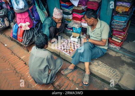 Bhaktapur, Nepal, um Juni 2012: Drei einheimische Männer sitzen vor dem Geschäft auf dem Boden und spielen Schach in Bhaktapur, Nepal. Dokumentarisches Editorial Stockfoto