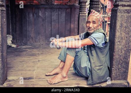 Bhaktapur, Nepal, um Juni 2012: Einheimischer Mann in blauen Kleidern und Kappe auf dem Kopf sitzt auf dem Boden und beugt sich auf Holzsäulen in Bhaktapur, Nepal. Stockfoto