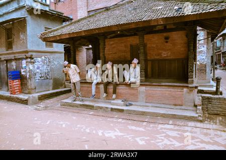 Bhaktapur, Nepal, um Juni 2012: Vier einheimische Männer mit traditionellen Kappen auf Köpfen sitzen und reden draußen in Bhaktapur, Nepal. Dokumentarisches Editorial Stockfoto