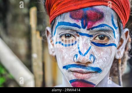 Silchar, Assam, um April 2012: Junge mit großen Augen und weißem Puder und blauen und roten Ornamenten im Gesicht trägt in Silchar, Assam, ein rotes Stirnband. Stockfoto