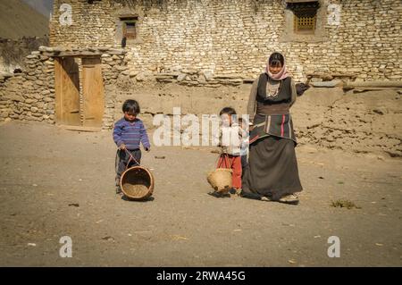 Dolpo, Nepal, um Juni 2012: Gebürtige Frau in braunem Kleid mit Kopftuch mit ihren zwei kleinen Kindern mit kleinen Körben in Dolpo, Nepal. Dokumentarfilm Stockfoto